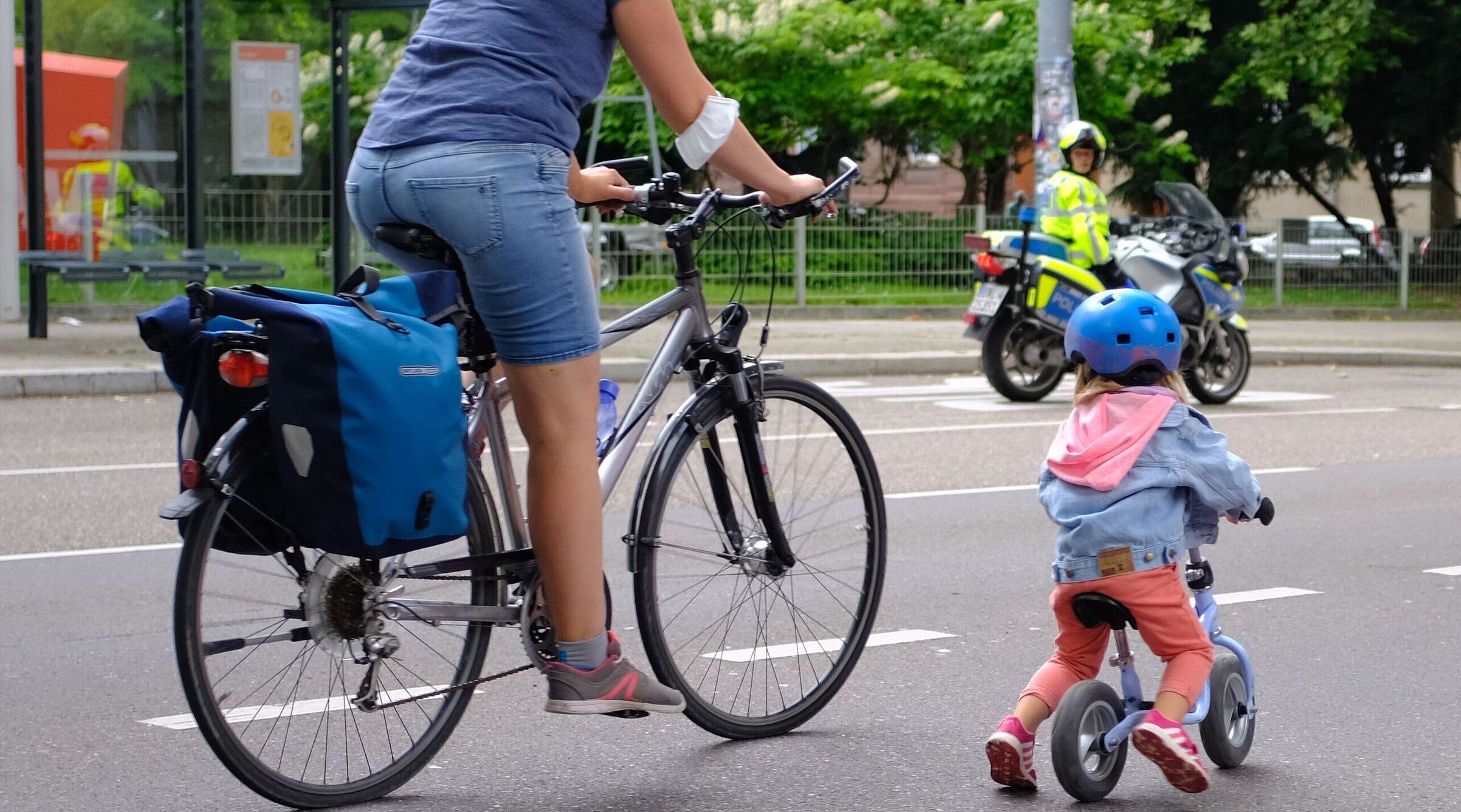 Mutter mit Kind auf der Straße. im Hintergrund ist ein Polizist zu sehen. 