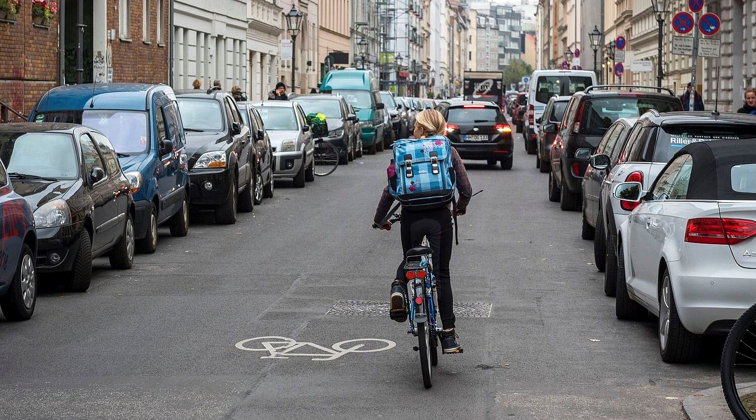 Mädchen auf dem Fahrrad fährt durch eine auf beiden Seiten zugeparkte Straße. 